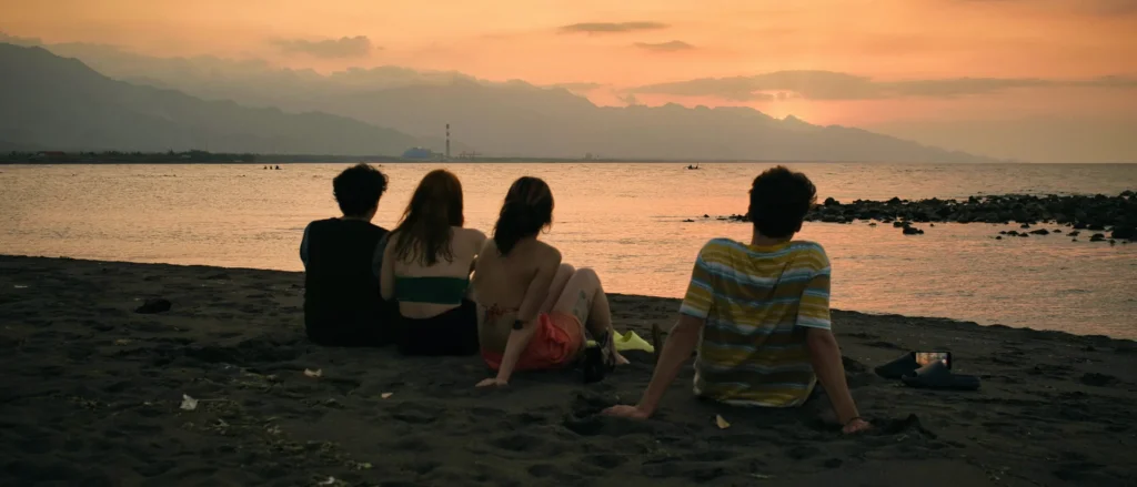 Groupe d'amis assis de dos face à la mer et aux montagnes, coucher de soleil orange, plage de Seririt, Bali