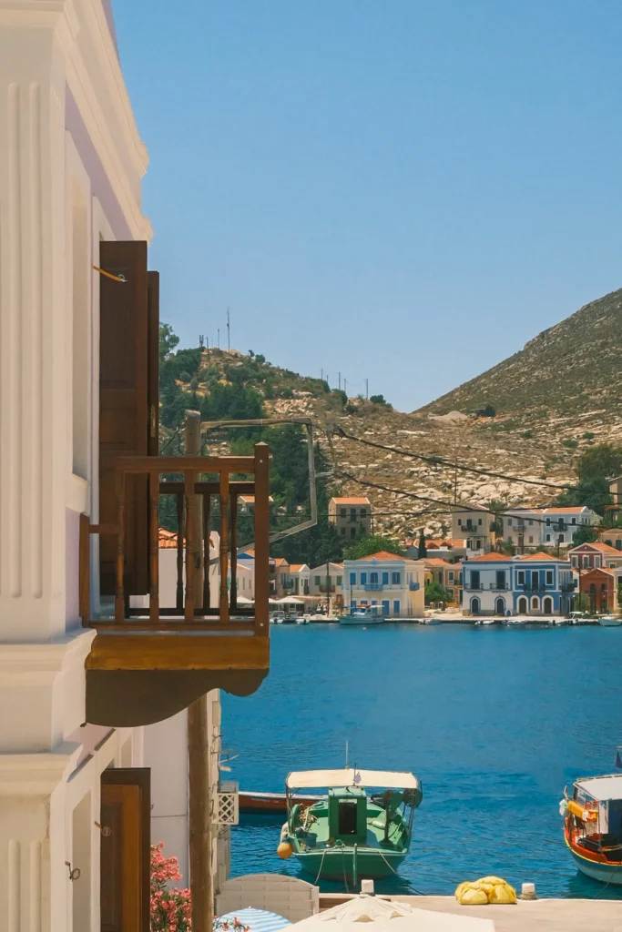Balcon en bois au premier plan face aux maisons colorées et bateaux du port de Kastellórizo, Grèce