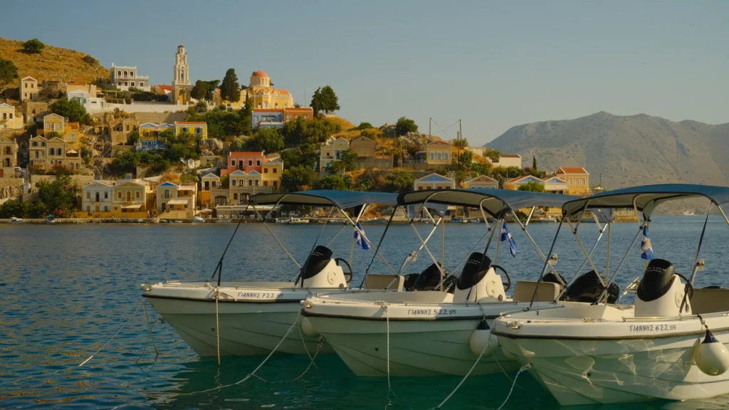 Trois canots à moteur amarrés au premier plan face aux maisons colorées et à l'église du port de Symi