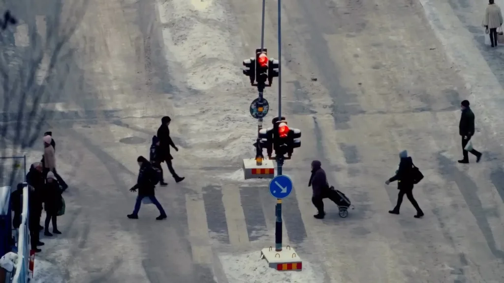 Vue en plongée d'un carrefour couvert de neige tassée, piétons traversant, feux de signalisation au premier plan