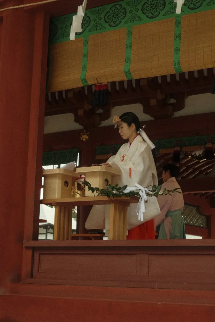 Jeune femme en tenue de miko dans la salle rouge d'un sanctuaire shinto pendant une cérémonie, Kyoto