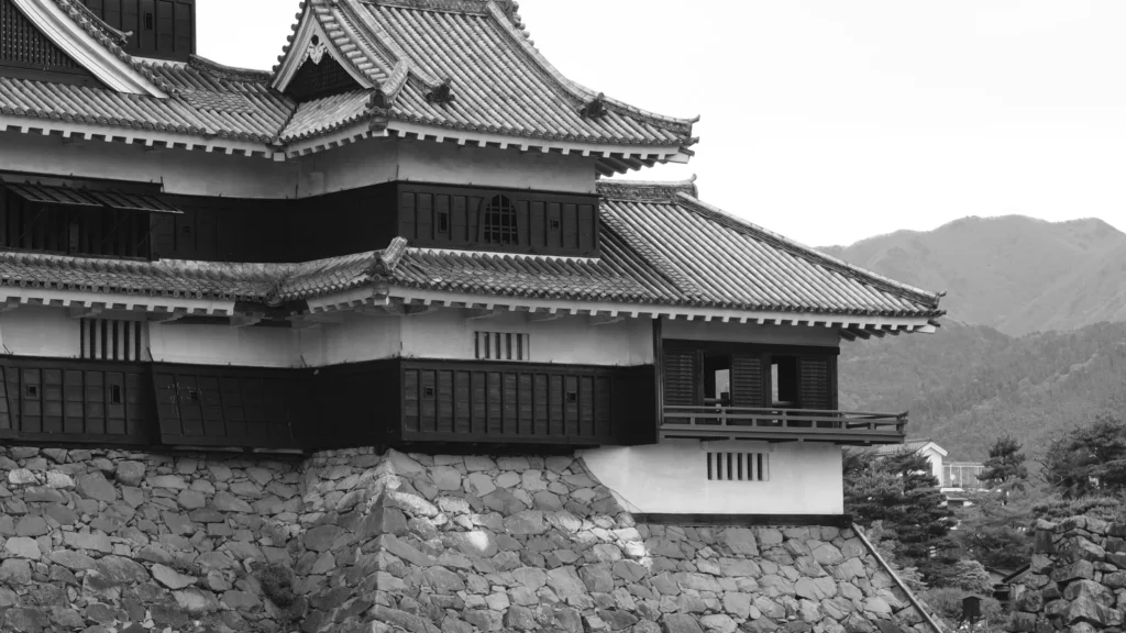 Détail des toits et du soubassement de pierre du château de Matsumoto en noir et blanc, montagnes à l'arrière-plan