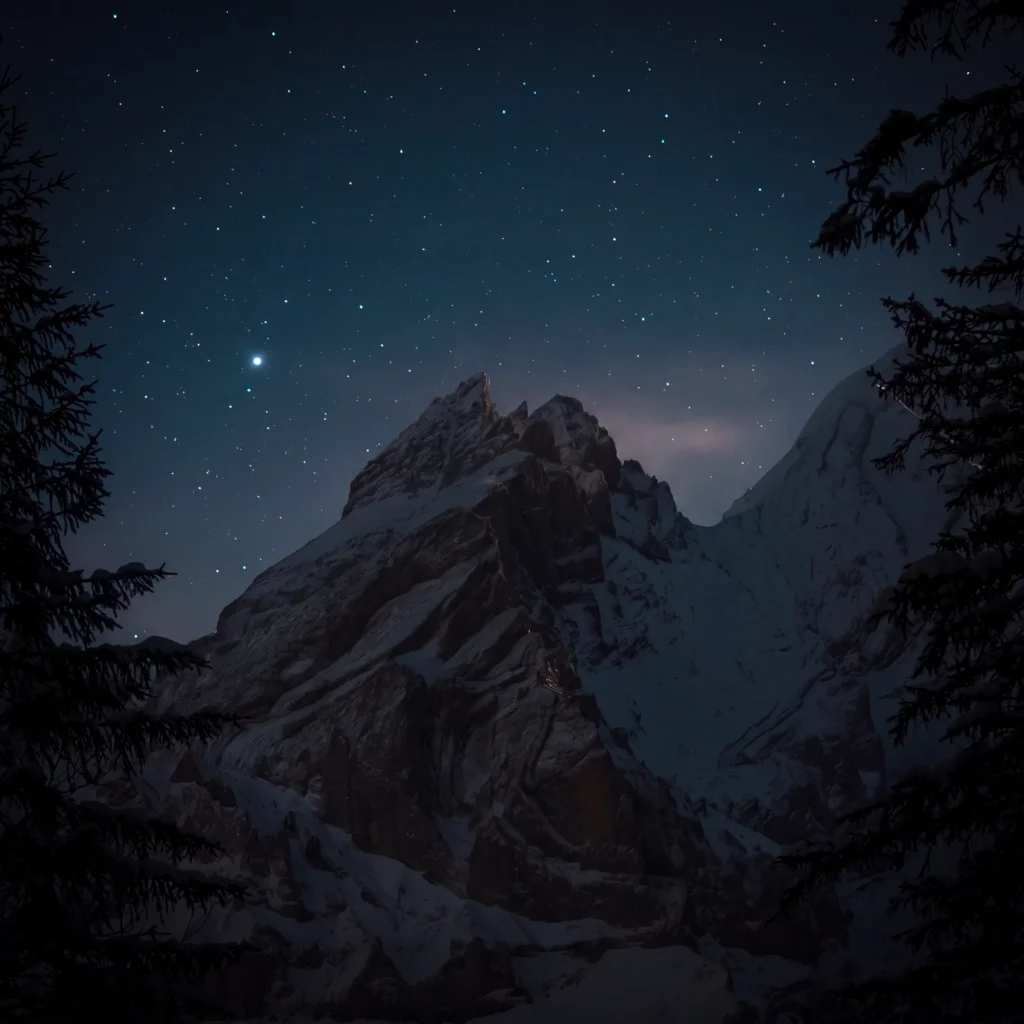 Ciel étoilé au-dessus d'un sommet rocheux et enneigé, encadré par des sapins, Suisse
