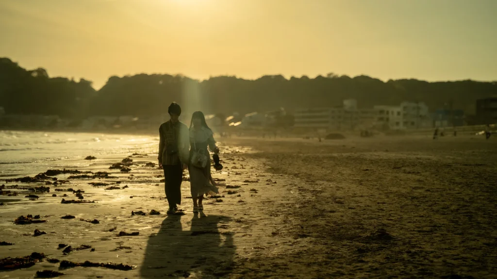 Deux silhouettes marchant sur une plage jonchée d'algues dans la lumière dorée du coucher du soleil