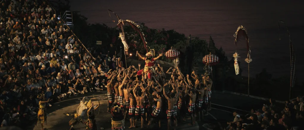Danseur en costume traditionnel porté par un groupe de danseurs torse nu en tenue à damier, spectacle de danse Kecak, Bali