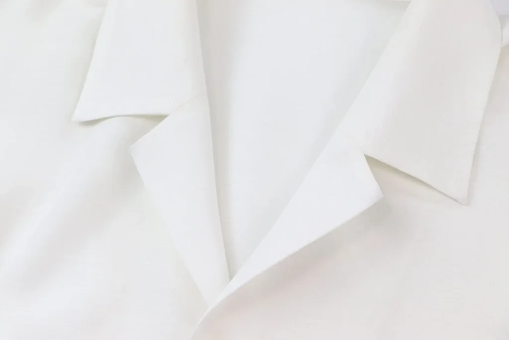 Gros plan sur le col et les manches d'une chemise blanche texturée signée Issey Miyake, plis et superpositions de tissu