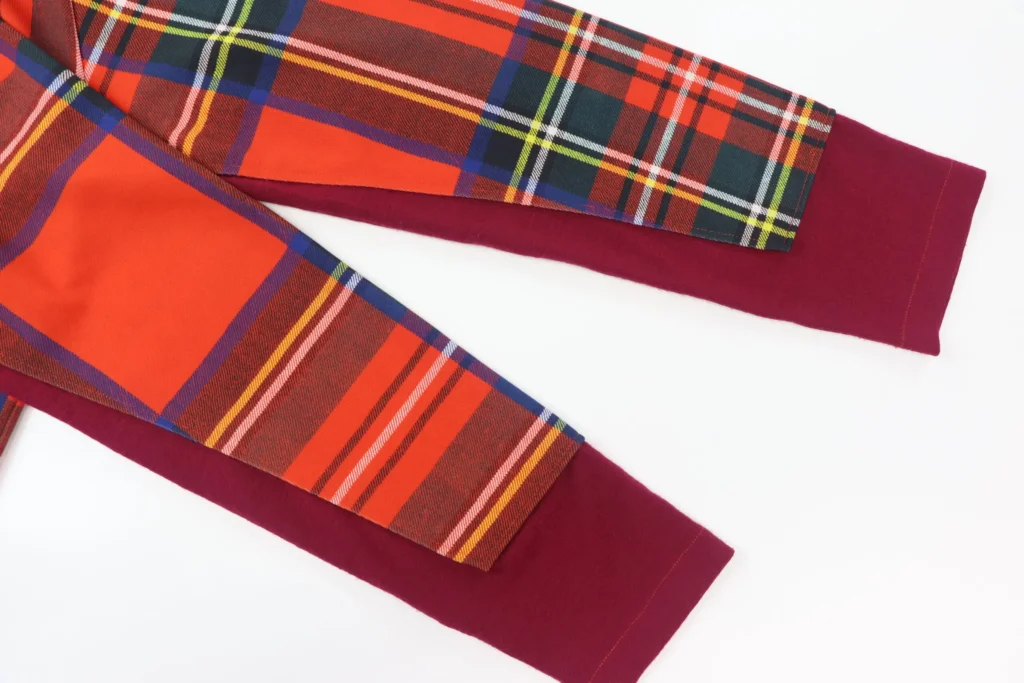 Gros plan sur les manches d'un pull tartan orange, vert et bleu signé Comme des Garçons des années 90, terminées par des poignets unis bordeaux