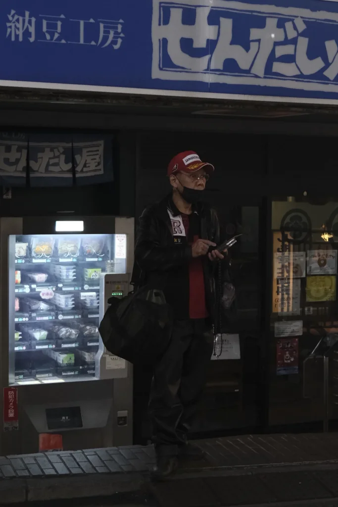 Homme devant un distributeur automatique lumineux dans une rue de nuit, Kōenji, Tokyo