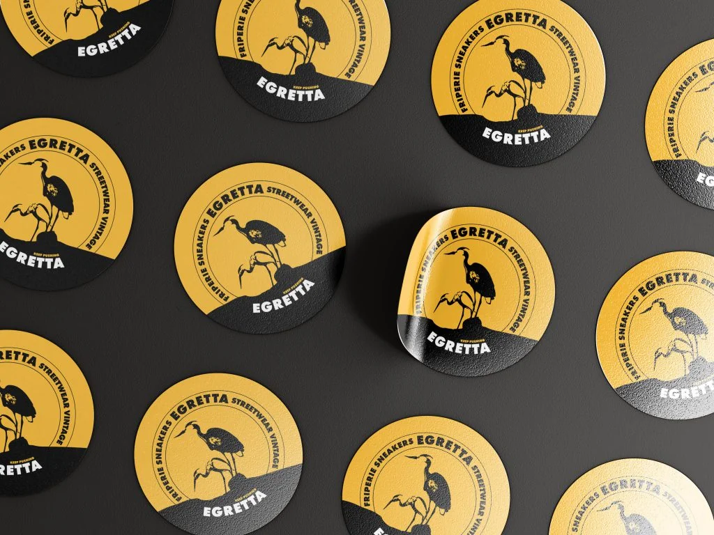 Mockup de stickers ronds Egretta noir et jaune, logo aigrette et mention "Friperie Sneakers Egretta Streetwear Vintage"