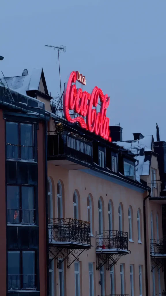 Enseigne néon rouge "Drick Coca-Cola" sur un toit d'immeuble enneigé à Slussen, ciel crépusculaire à Stockholm