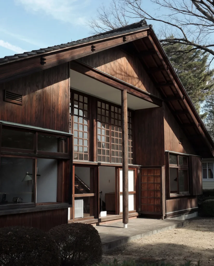 Façade en bois sombre d'une maison japonaise moderniste avec baies vitrées quadrillées et toit à pignon