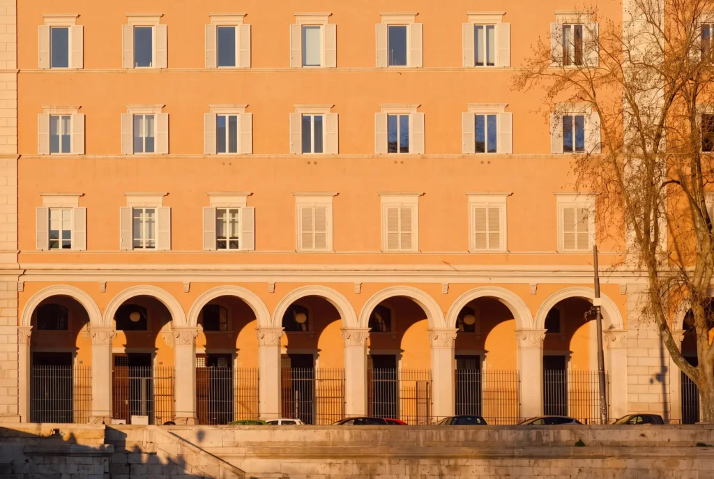 Facade d'immeuble orange avec rangees de fenetres a volets et rez-de-chaussee a arcades, voitures garees en contrebas