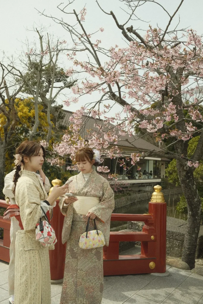 Deux femmes en kimono près d'un pont rouge entouré de cerisiers en fleurs, Japon