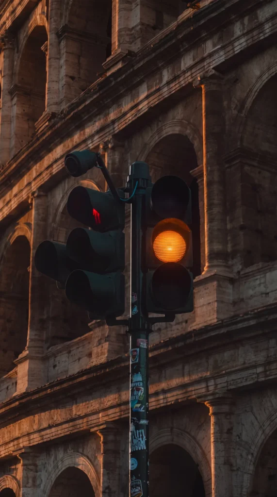 Feu de circulation orange allumé au premier plan devant les arches du Colisée à Rome, lumière du soir