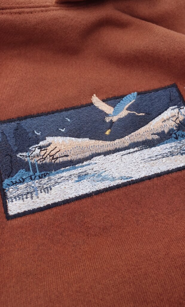 Gros plan sur un patch brodé représentant une aigrette survolant un paysage montagneux, hoodie Egretta