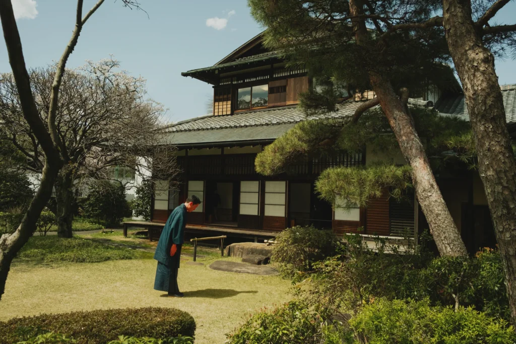 Homme en kimono sombre penché dans le jardin d'une maison japonaise traditionnelle entourée de pins