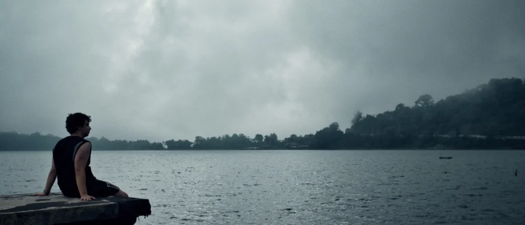 Homme assis sur un ponton en bois face à un lac brumeux entouré de forêt, près du temple Ulun Danu Beratan, Bali