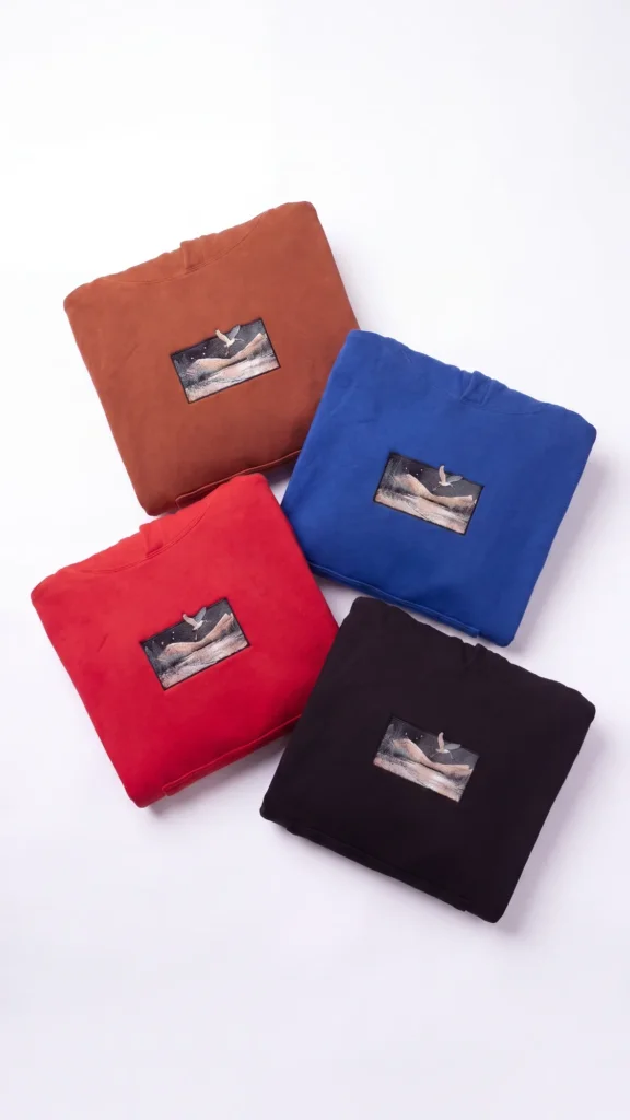 Quatre hoodies Egretta pliés en orange brique, bleu, rouge et noir, patch brodé aigrette sur chacun
