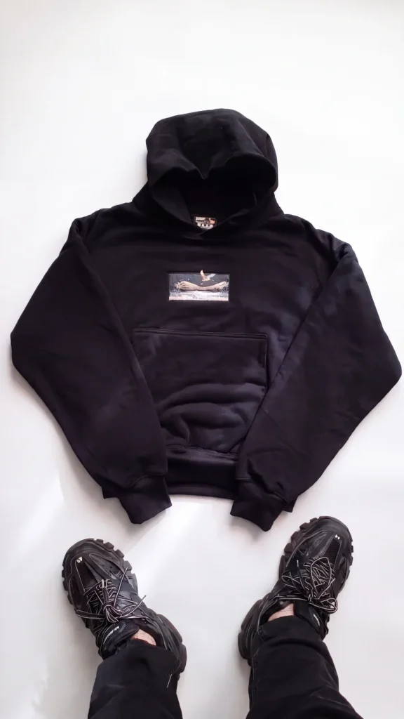 Hoodie Egretta noir posé à plat avec patch brodé, porté avec sneakers noires