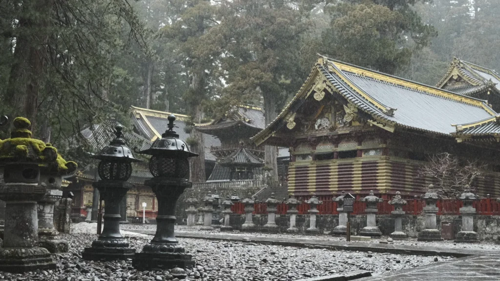Lanternes de pierre et pavillon aux toits dorés du sanctuaire Tōshō-gū sous une neige légère, Nikkō