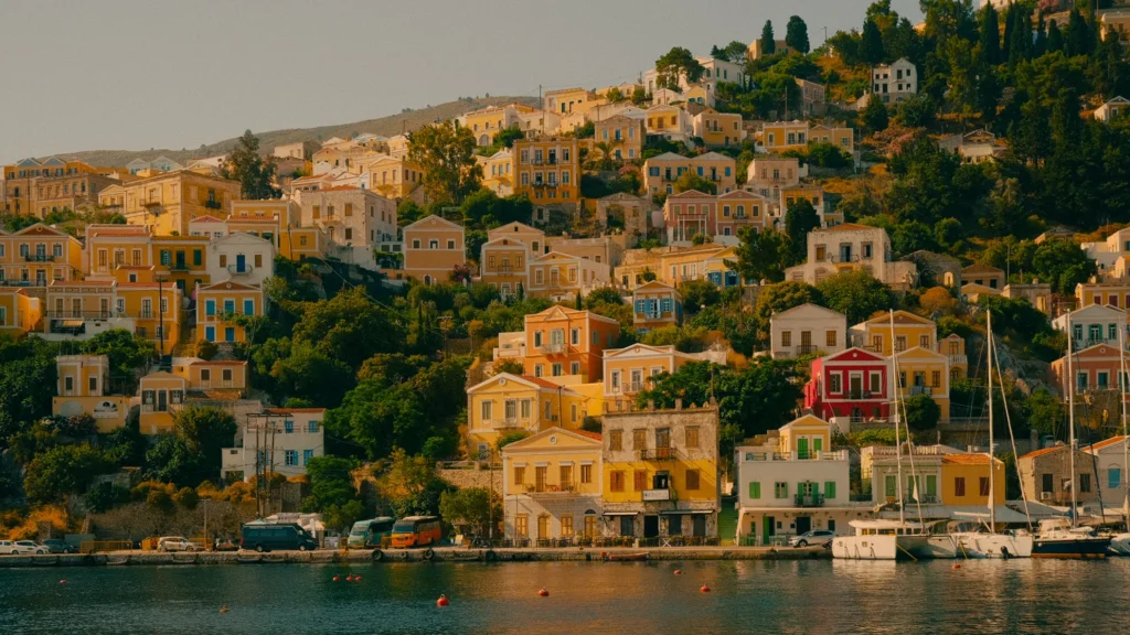 Maisons néoclassiques jaunes, oranges et rouges étagées à flanc de colline au-dessus du port de Symi