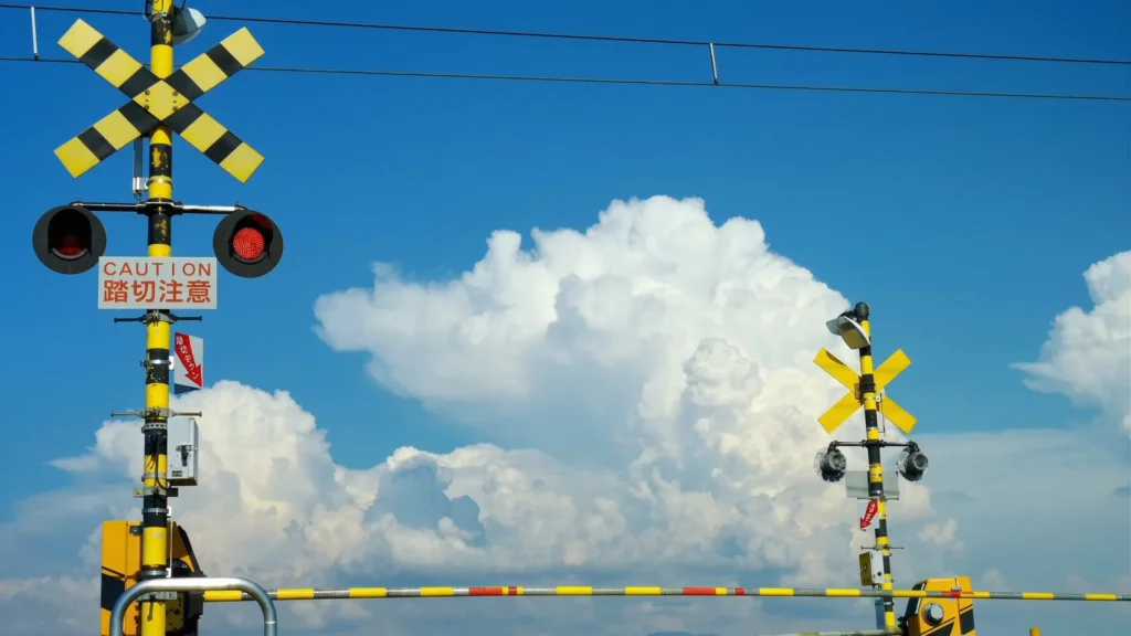 Passage à niveau jaune et noir avec feux rouges sous un grand ciel bleu et de gros nuages blancs