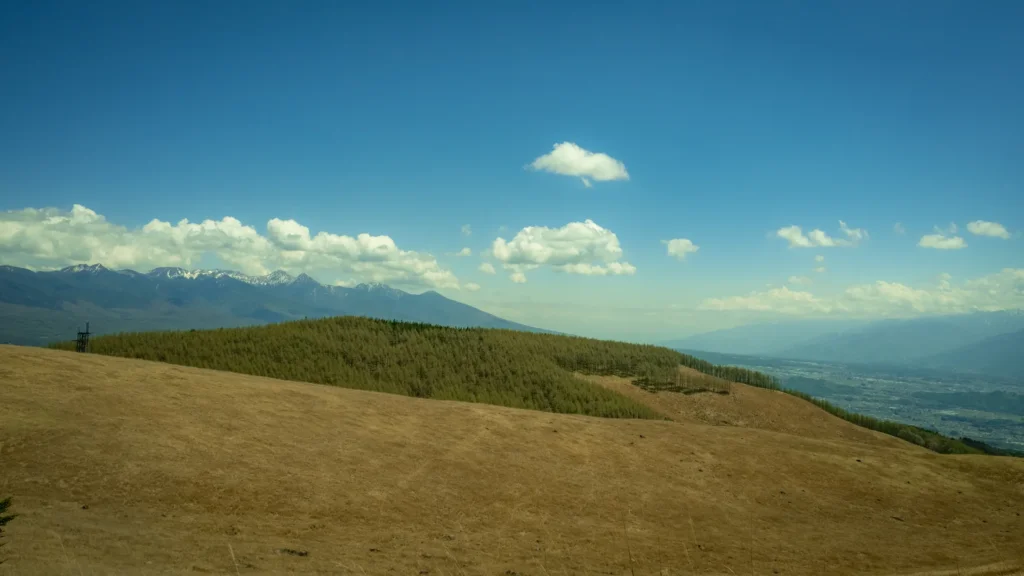 Pente d'herbes sèches face à une vallée et aux sommets des Alpes japonaises sous un ciel bleu