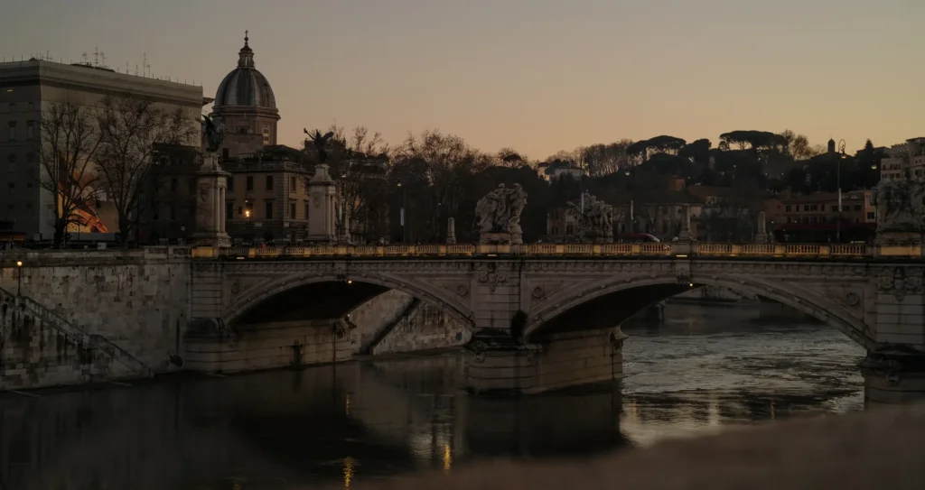Vue du pont Vittorio Emanuele II et de ses statues de Victoires ailées sur le Tibre, dôme de San Giovanni dei Fiorentini en arrière-plan, ciel orangé au crépuscule