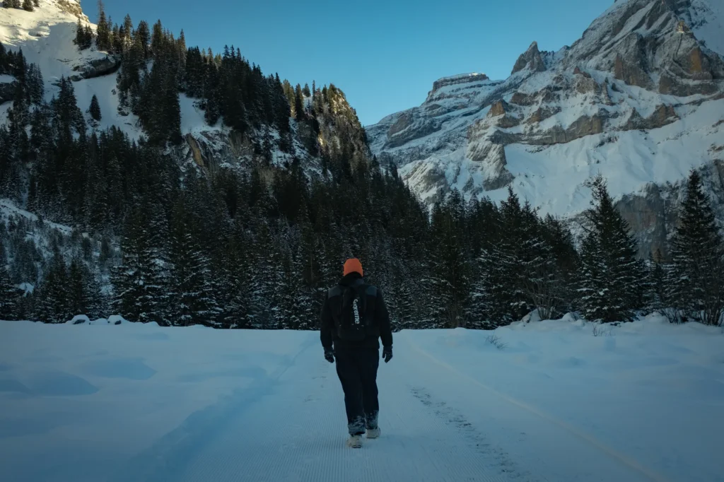 Randonneur de dos marchant dans la neige face aux sommets enneigés de Kandersteg, en Suisse
