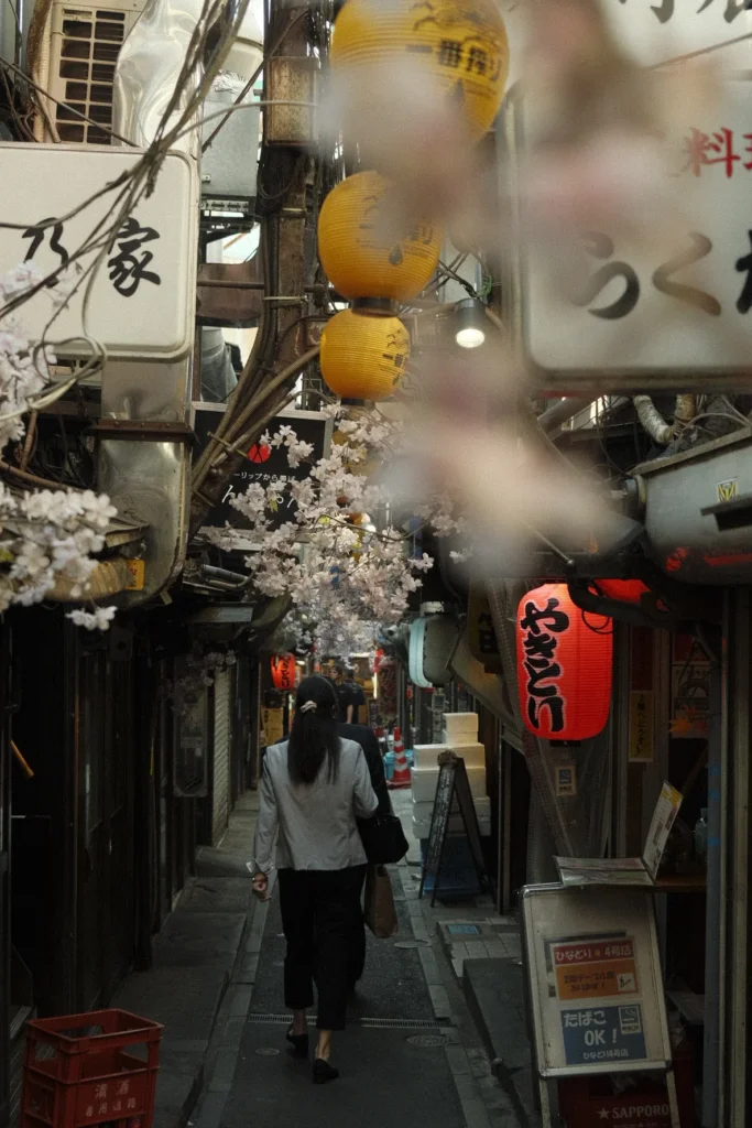 Étroite ruelle de bars avec lanternes allumées et branches de cerisier en fleurs, près de la gare de Shinjuku, Tokyo