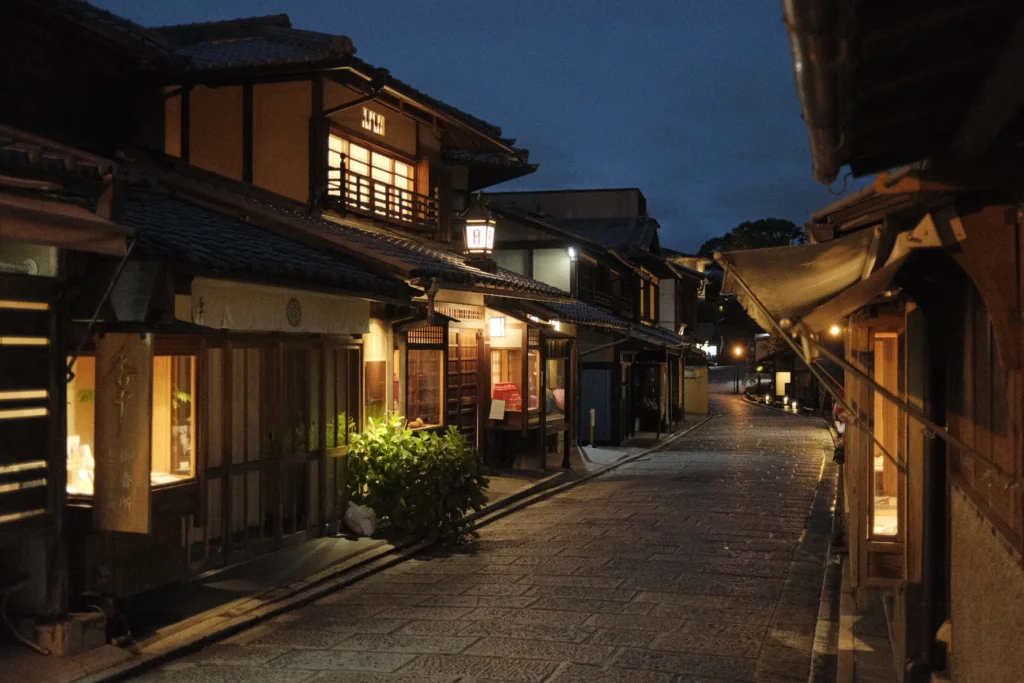 Ruelle pavée bordée de maisons de bois traditionnelles éclairées au crépuscule, Kyoto