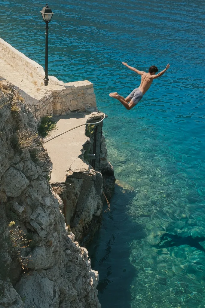 Homme sautant depuis une falaise rocheuse dans une mer turquoise transparente, port de Kastellórizo