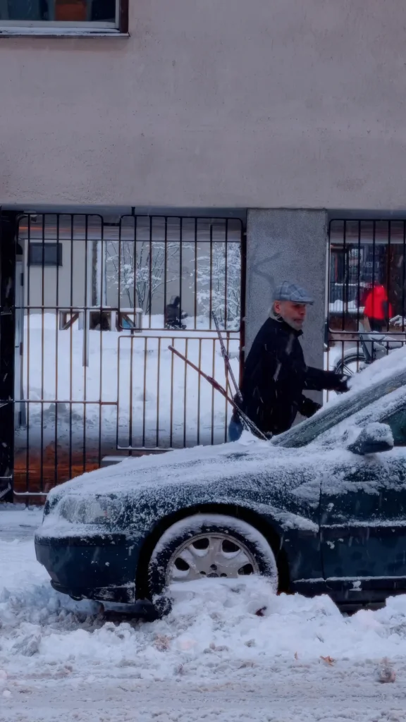 Homme déneigeant sa voiture recouverte de neige dans une rue résidentielle de Stockholm, en hiver