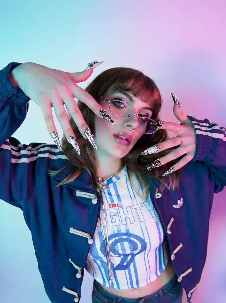 Portrait en studio, veste et bas de jogging Adidas bleu marine à bandes, crop top rayé, lunettes ovales, manucure griffée argentée