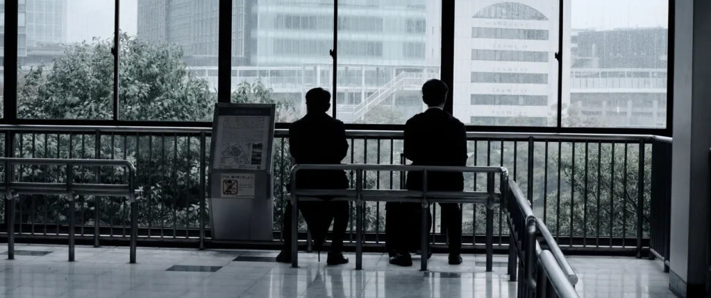 Deux hommes en silhouette assis sur un banc, vus à travers des vitres, Tokyo