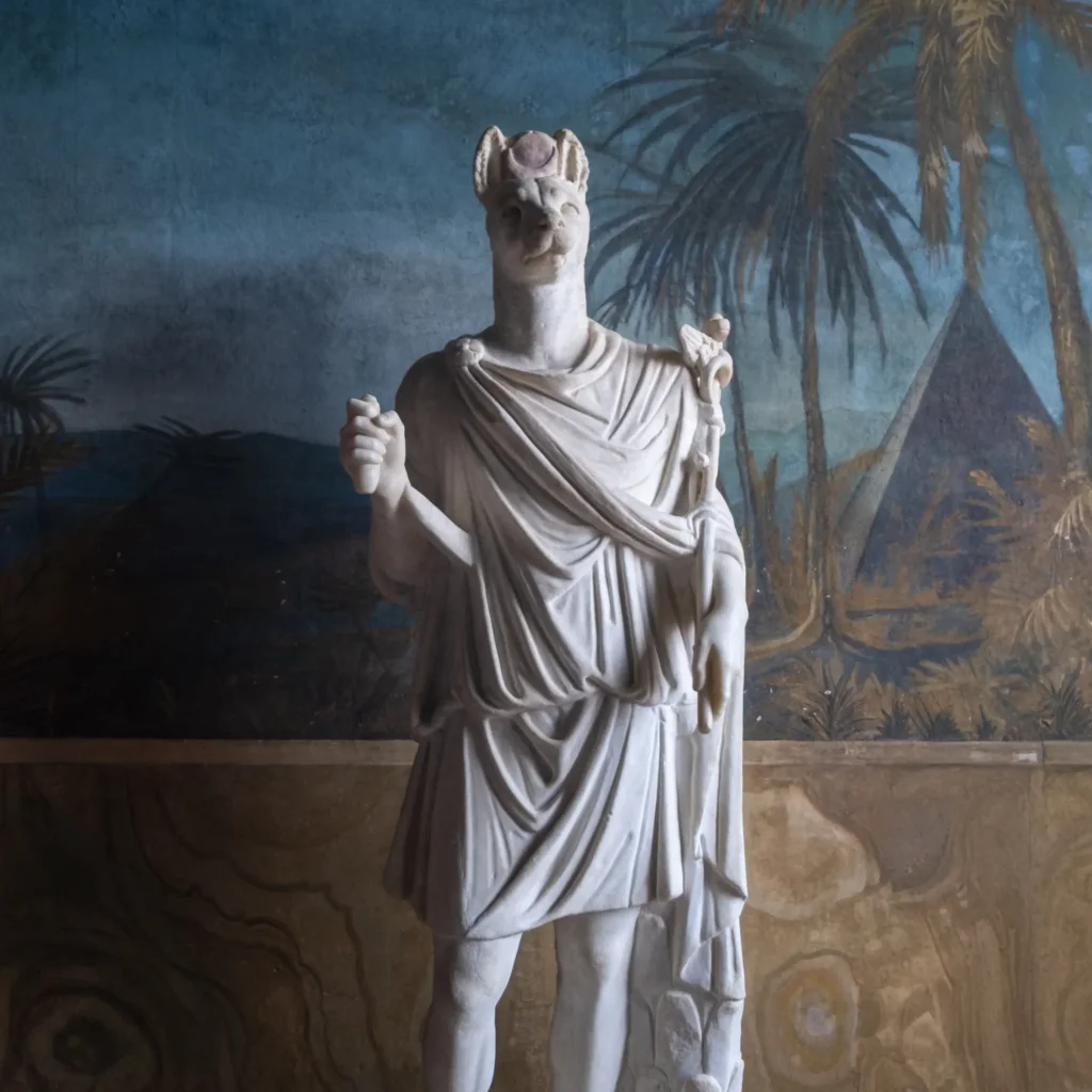 Statue en marbre d'Hermanubis, divinité à tête de chacal drapée à la romaine, tenant un caducée, devant une fresque égyptisante